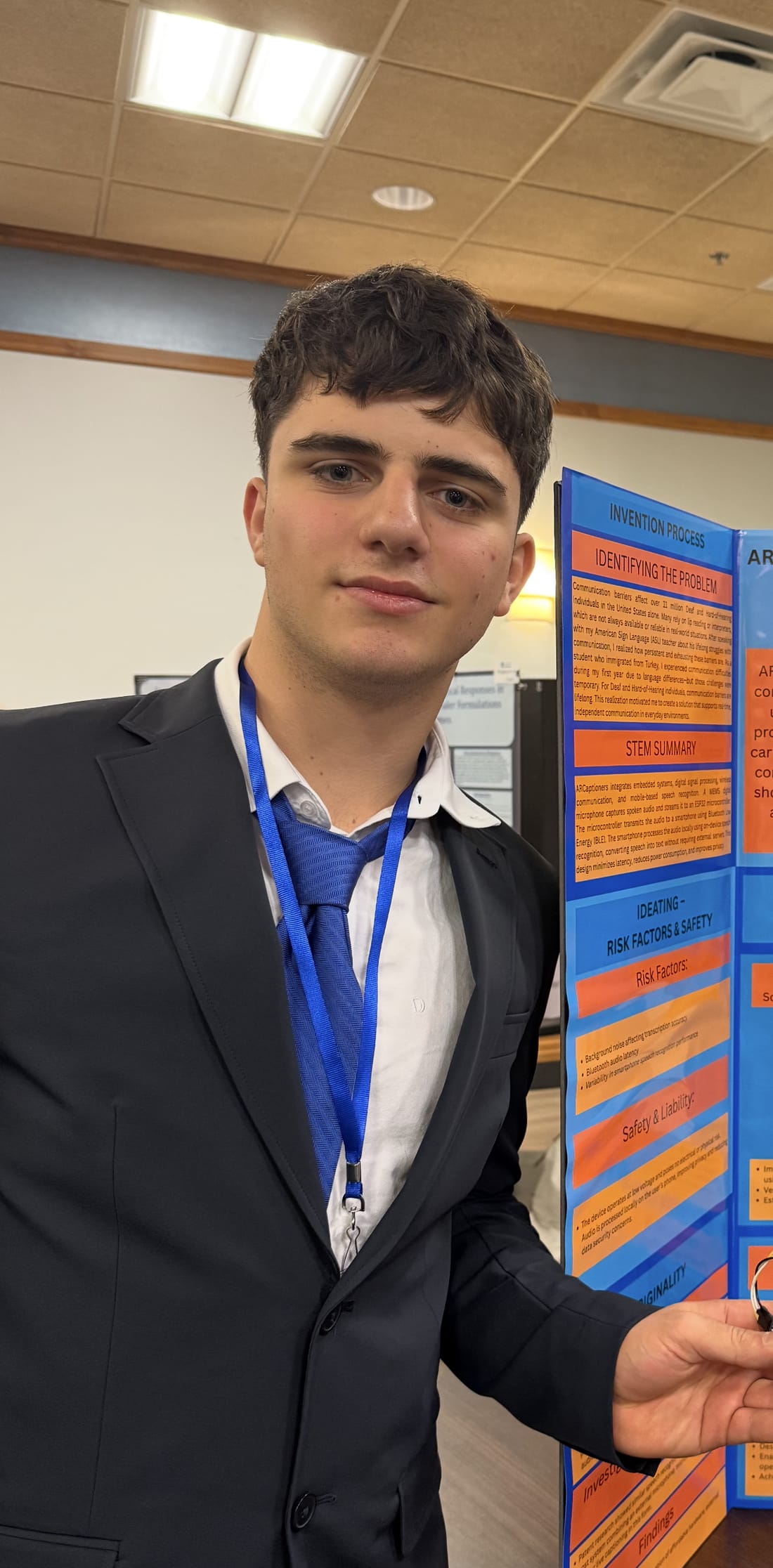 Stephan in a suit presenting the AR Captioners project board at the Edison Regional Inventors Fair